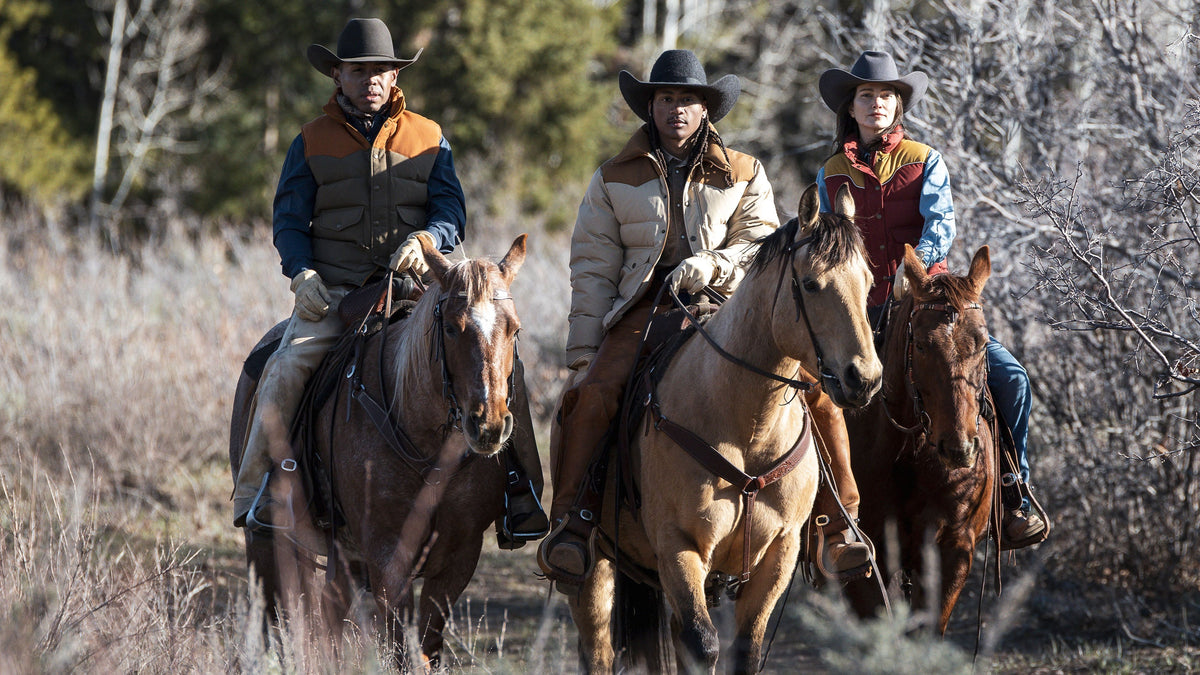 Three cowboys riding horses through a wooded area