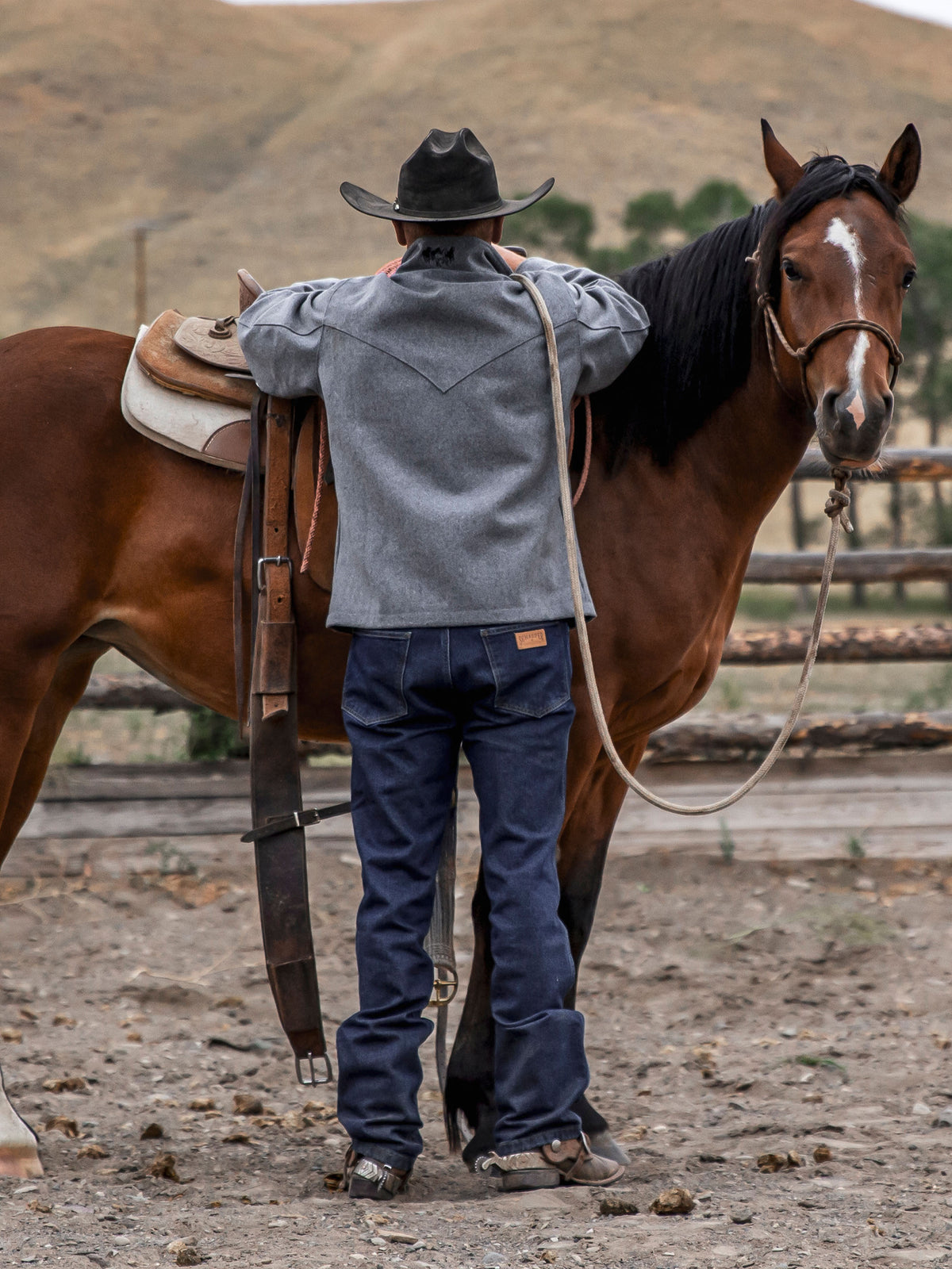Blue denim dungarees on a man with boots, standing beside a horse.