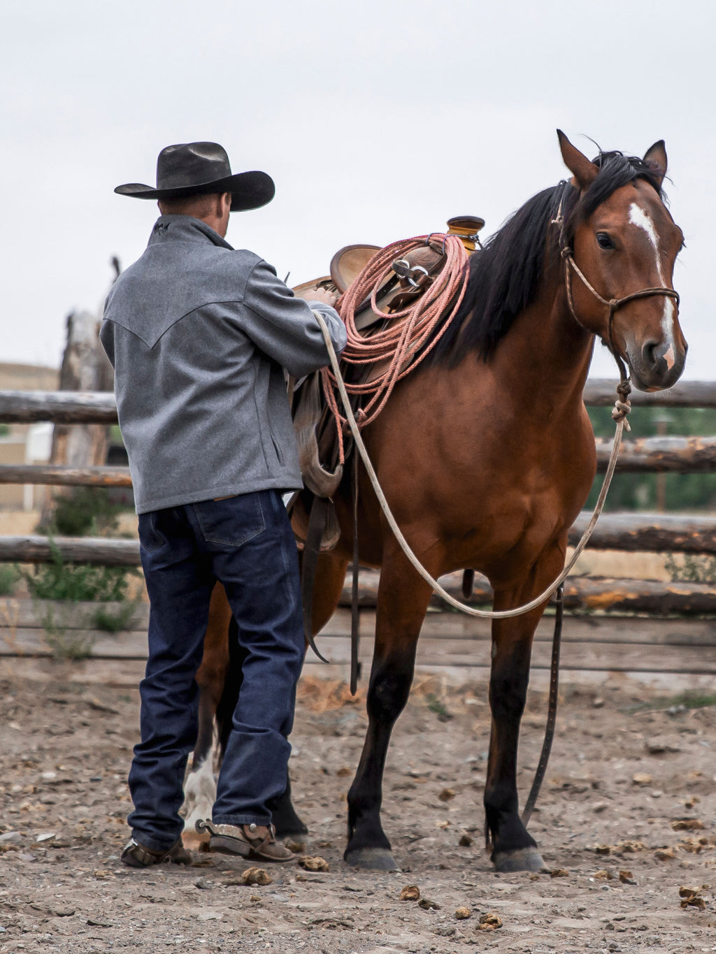 Blue denim dungarees on a man with boots, facing away beside a horse.