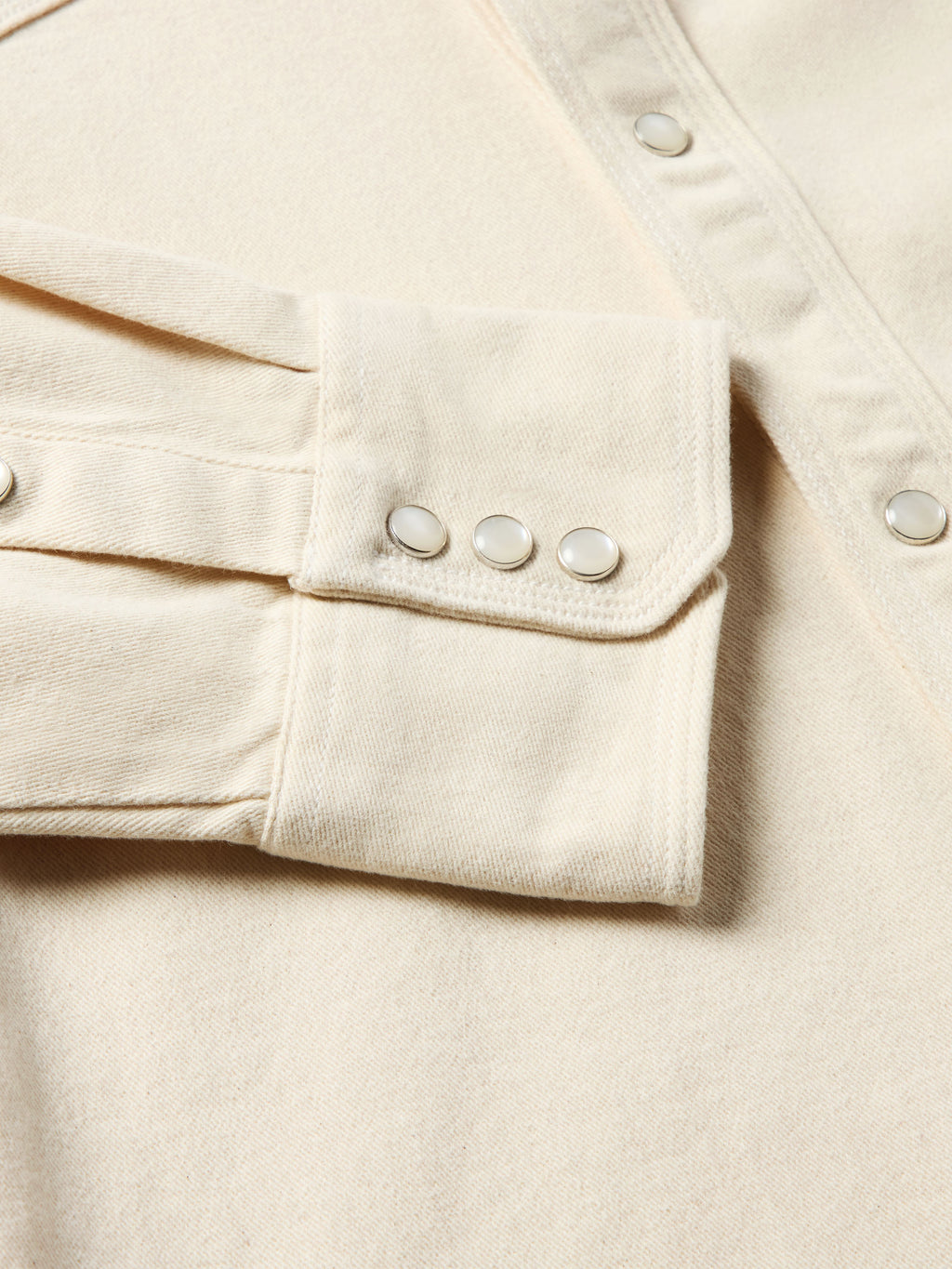 Natural denim snap shirt sleeve cuff detail with snap cuff and reinforced seam stitching