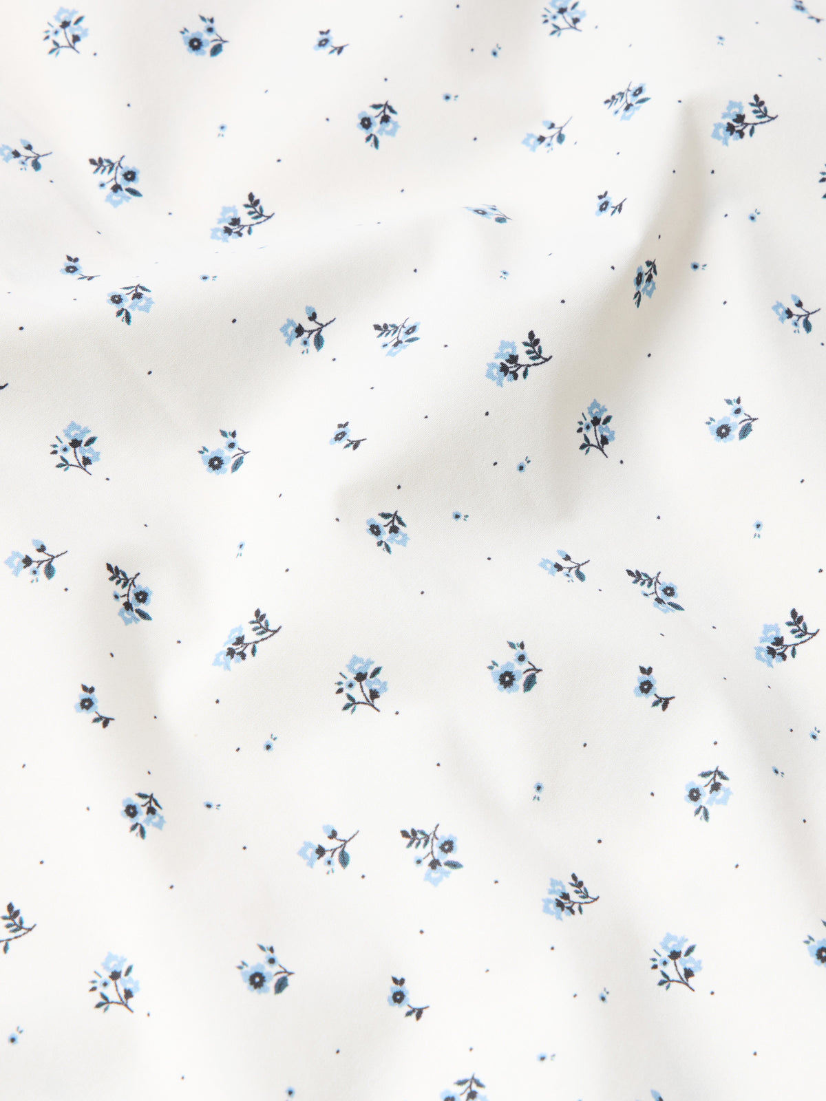 Close-up of white fabric with small blue floral dot pattern for short-sleeve pearl snap shirt.
