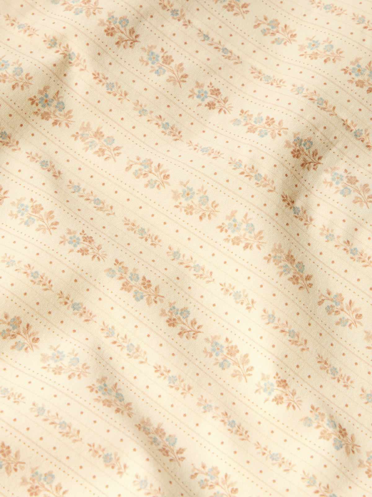 Close-up of light cream western shirt fabric with small floral print and stitched lines.