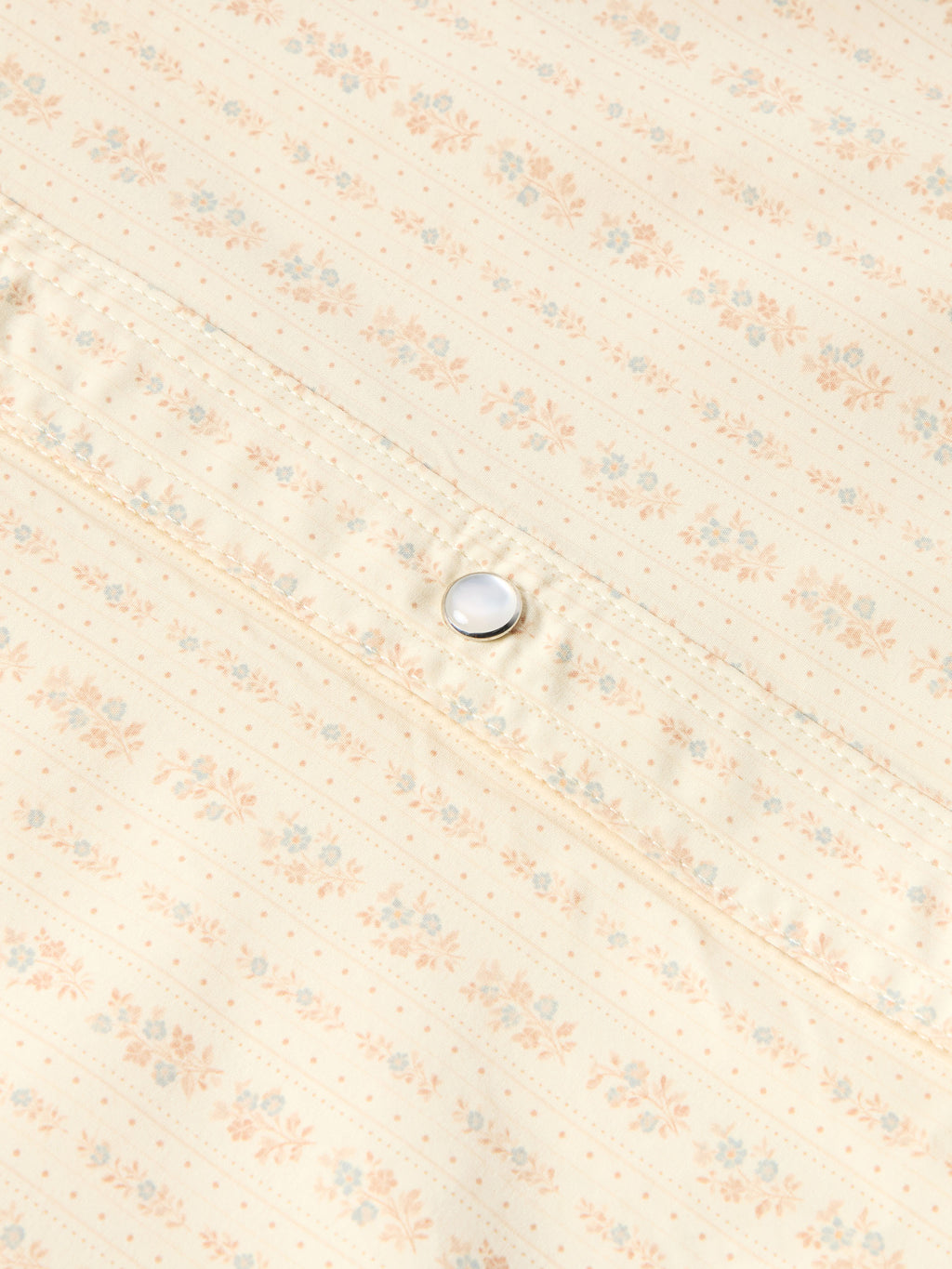 Close-up of round pearl snap button on light cream patterned western shirt.