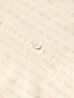 Close-up of round pearl snap button on light cream patterned western shirt.