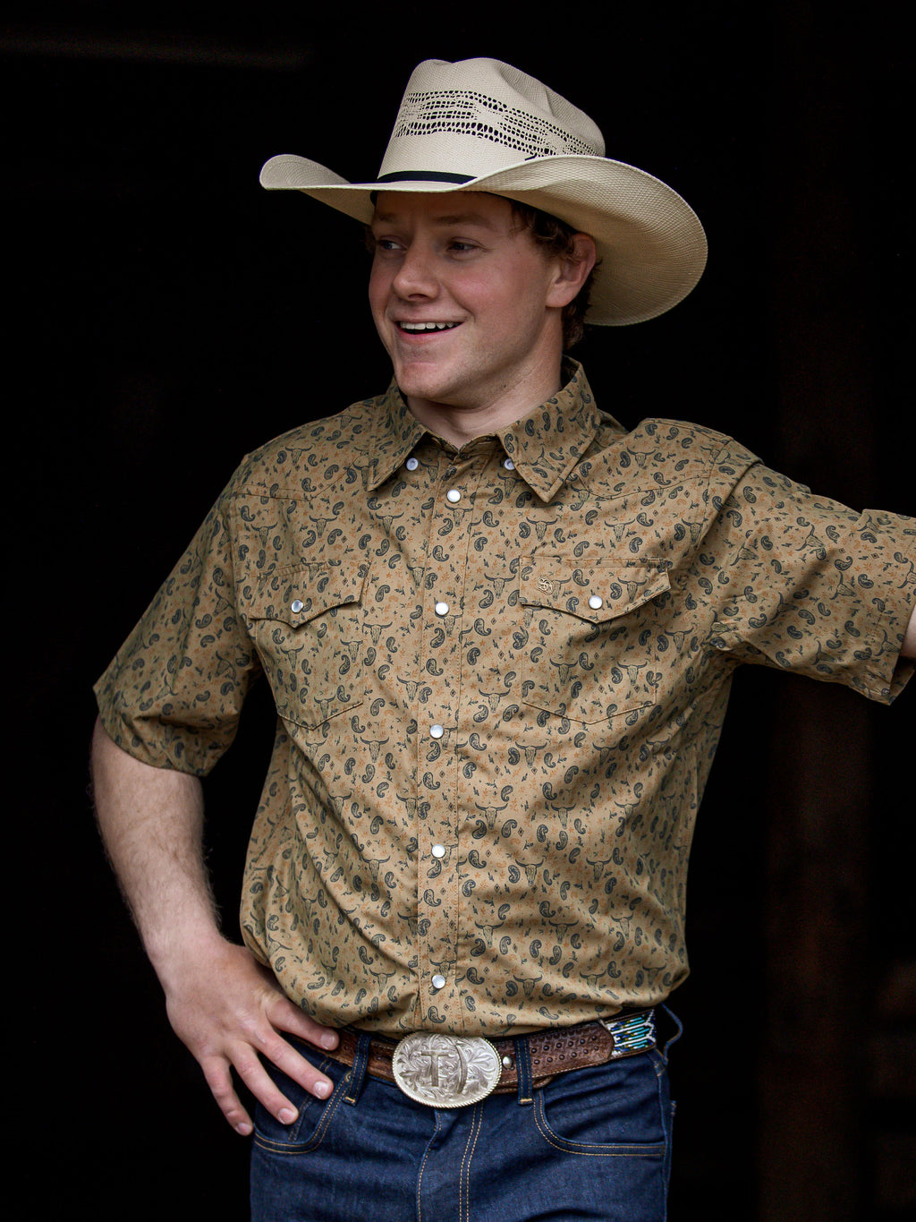 Western short sleeve shirt with pearl snap buttons and chest pockets; patterned tan print.