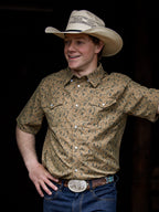 Western short sleeve shirt with pearl snap buttons and chest pockets; patterned tan print.
