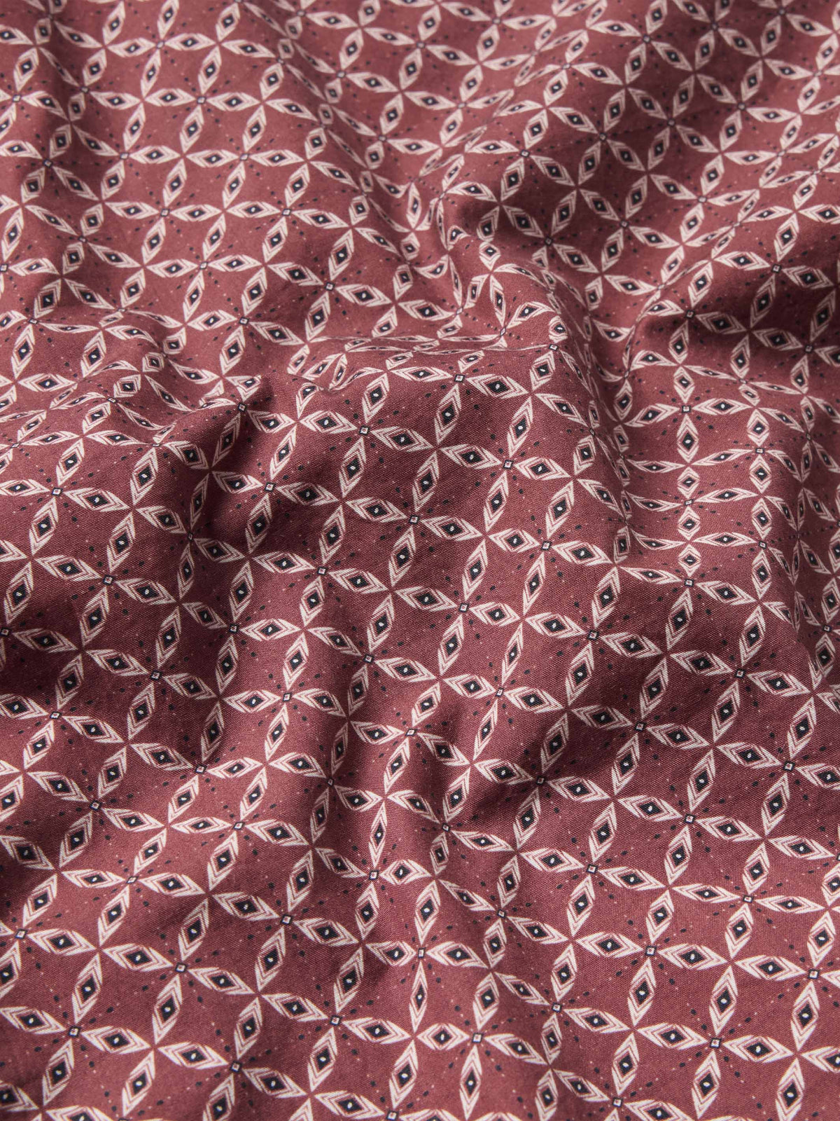 Dark red cotton snap shirt fabric with repeating small geometric pattern, close-up view.