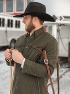 Olive wool overshirt with button front and flap pockets, styled with brown leather straps.