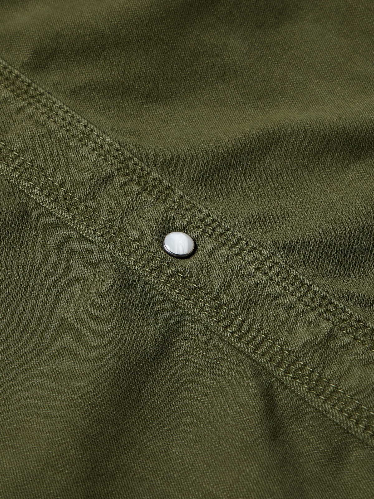 Dark olive denim snap shirt sleeve seam with white snap button