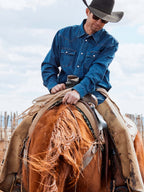 Dark indigo denim snap shirt worn by cowboy, snap front and collar visible
