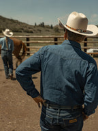 Dark indigo denim snap shirt worn by cowboy, back yoke and snap detail visible