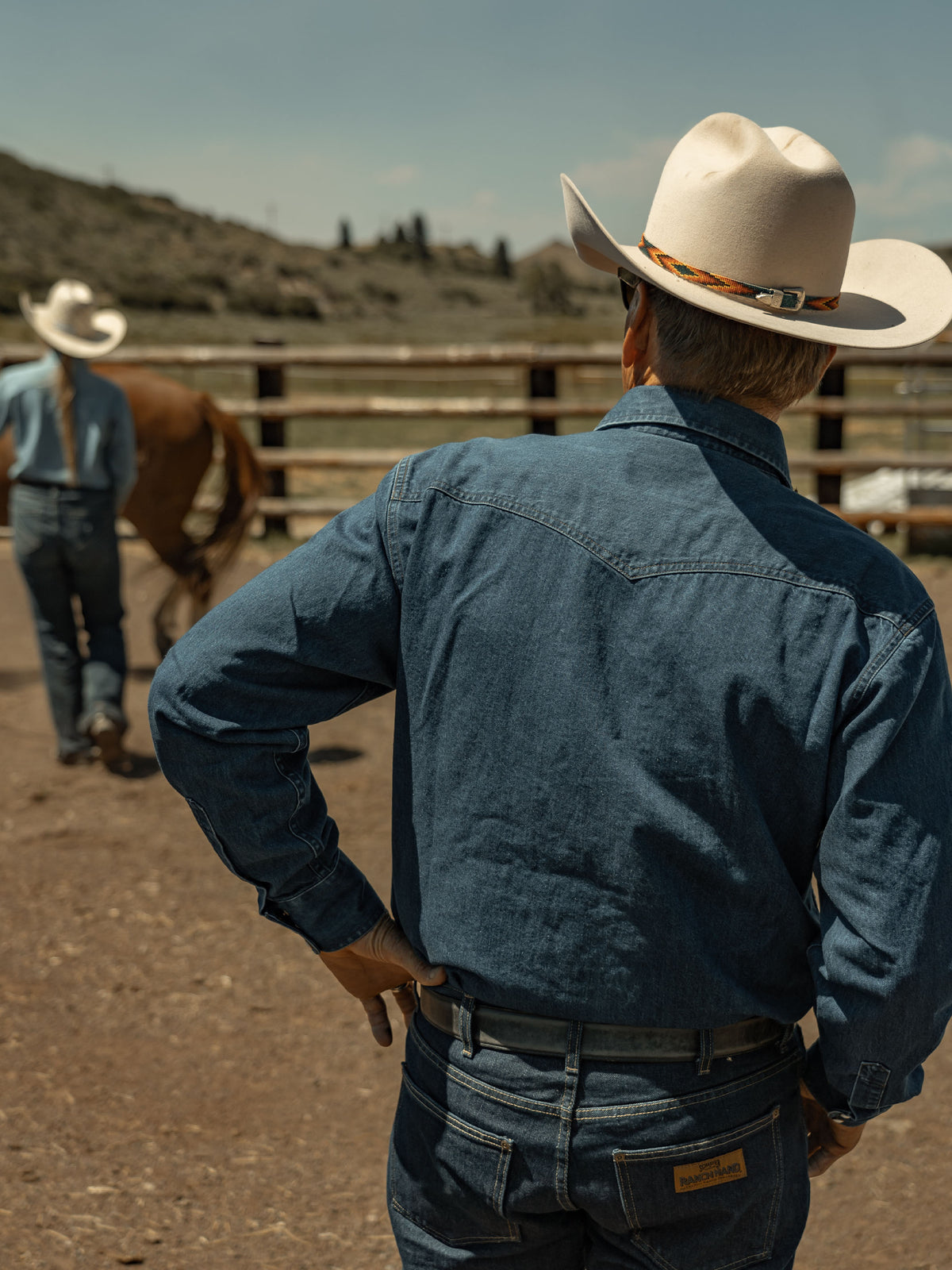 Dark indigo denim snap shirt worn by cowboy, back yoke and snap detail visible