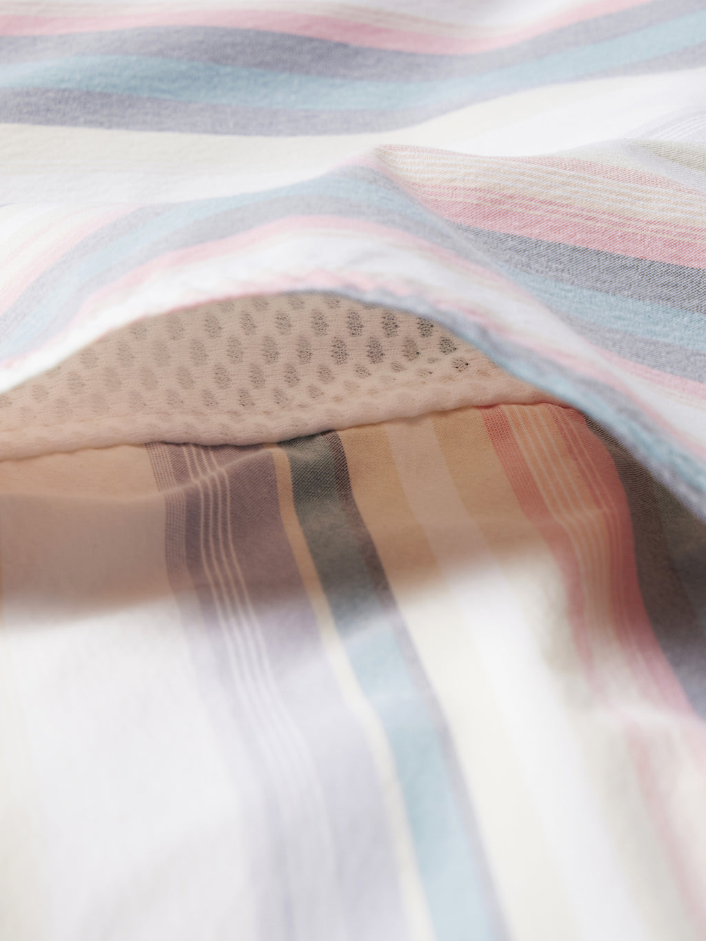 Close-up of pastel striped fabric in light blue, pink, and white with stitched trim