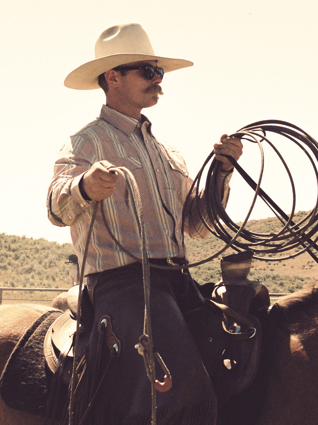 Men's pink striped button-up shirt on model with cowboy hat and saddle gear
