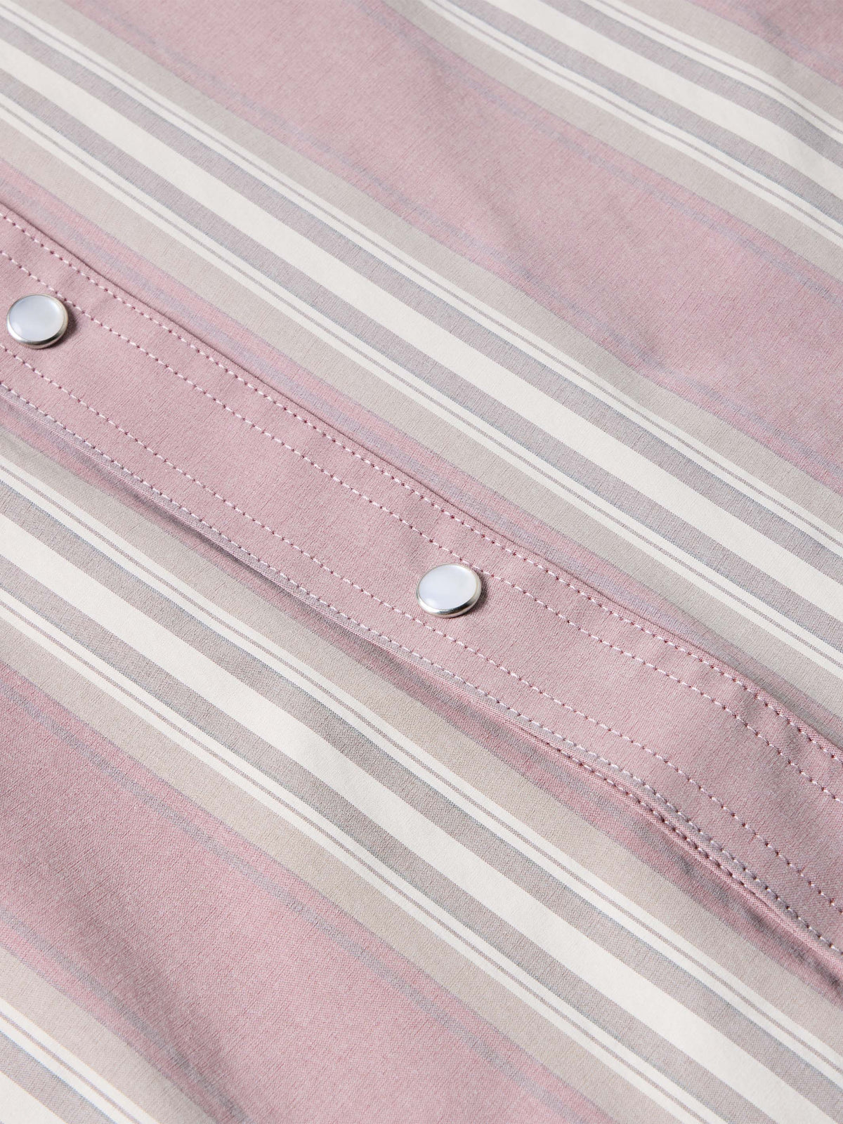 Pink striped shirt fabric close-up with rows of stitching and metal buttons