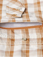 Close-up of tan-and-white plaid western snap shirt hem with metal snap placket.