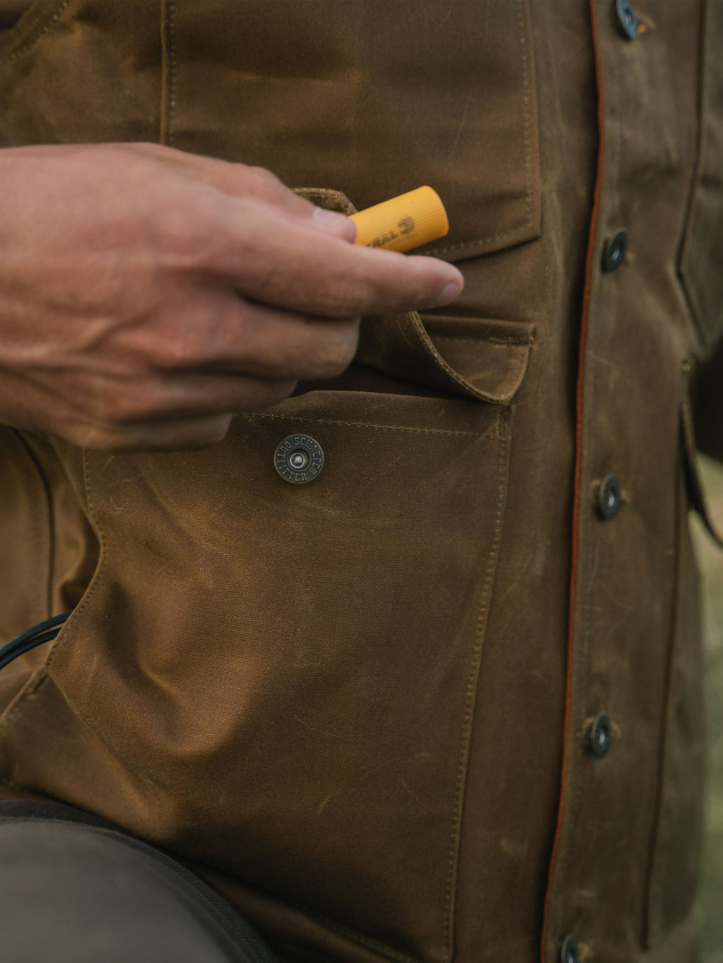 RangeWax® Mesquite vest pocket close-up with hand inserting an orange tool.