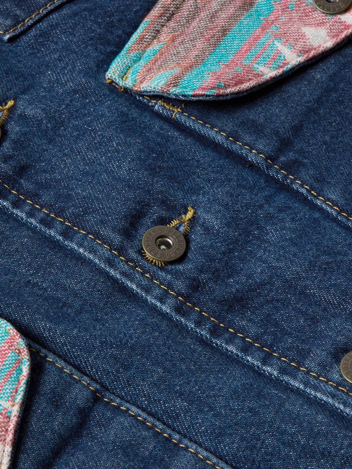 Close-up of blue denim vest with metal buttons and colorful stitched pocket flap