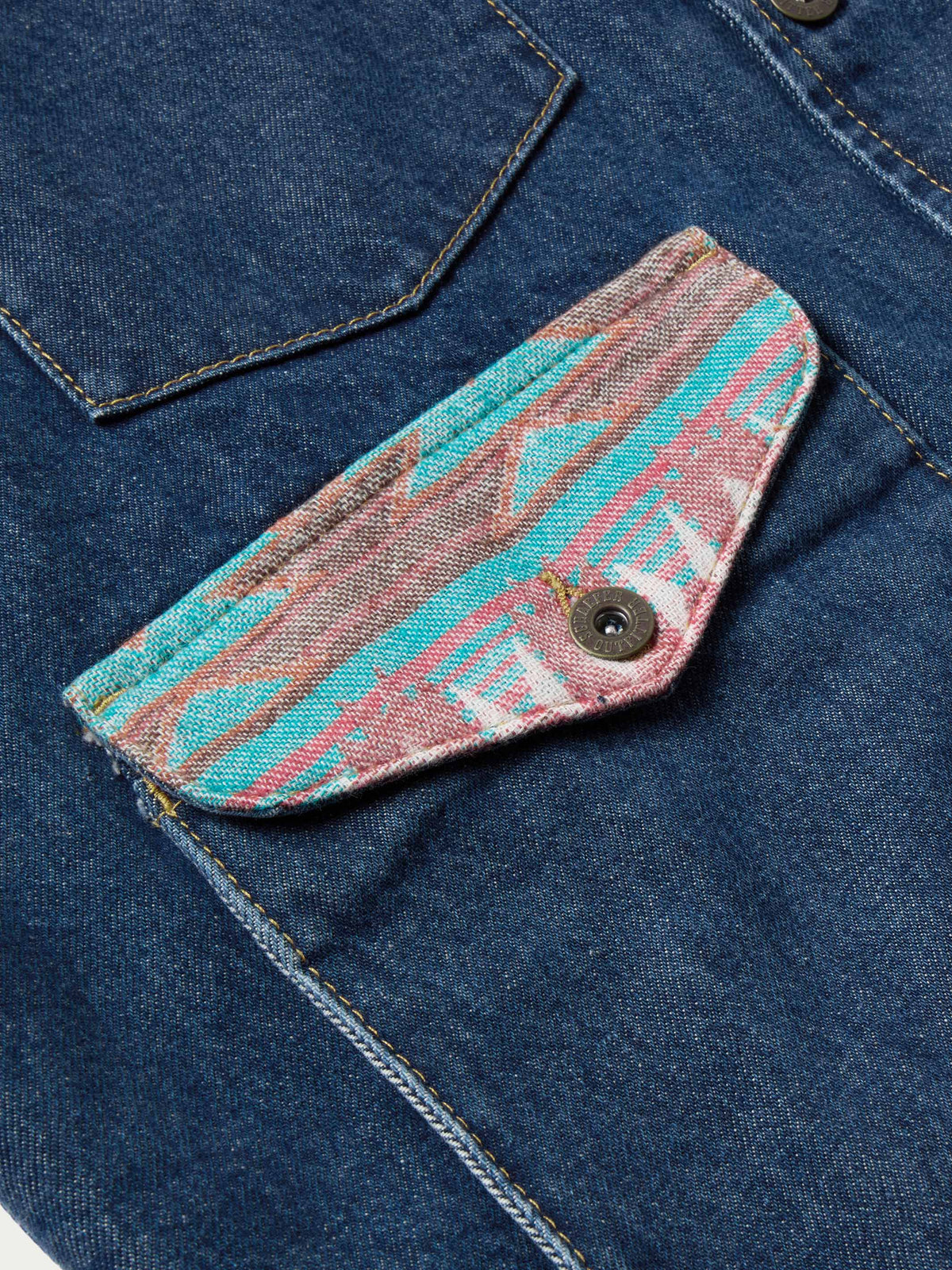 Close-up of blue denim pocket flap with round button and colorful textile trim