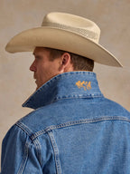 Medium indigo denim jacket showing back yoke with small yellow/orange embroidered patch