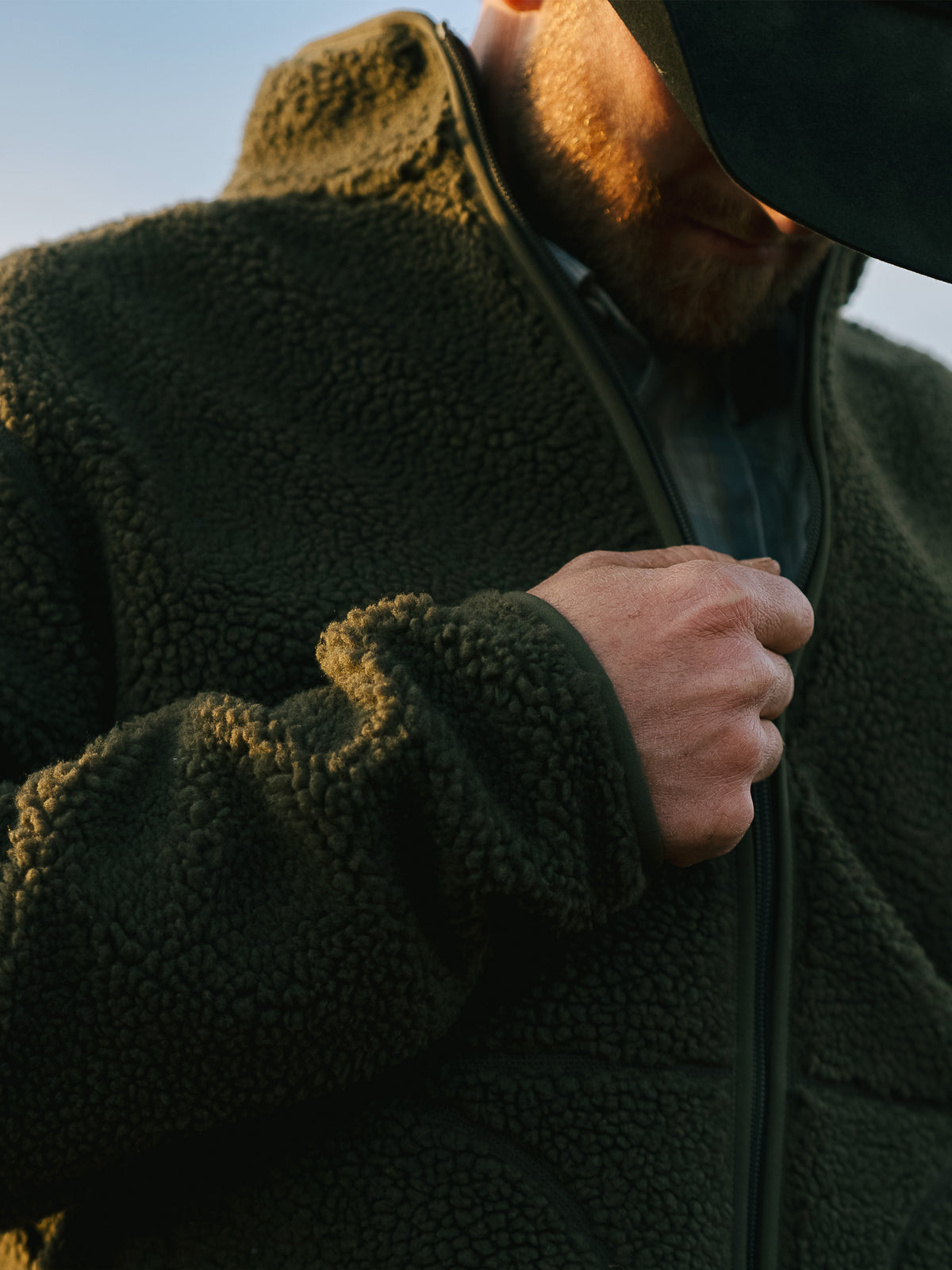 Olive full-zip fleece jacket on a man outdoors, high collar and sherpa-like texture.