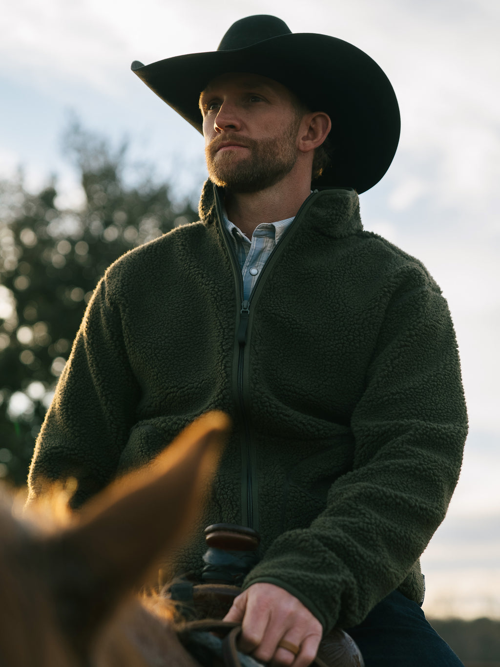 Olive full-zip fleece jacket on a man outdoors with high collar and plush fabric.