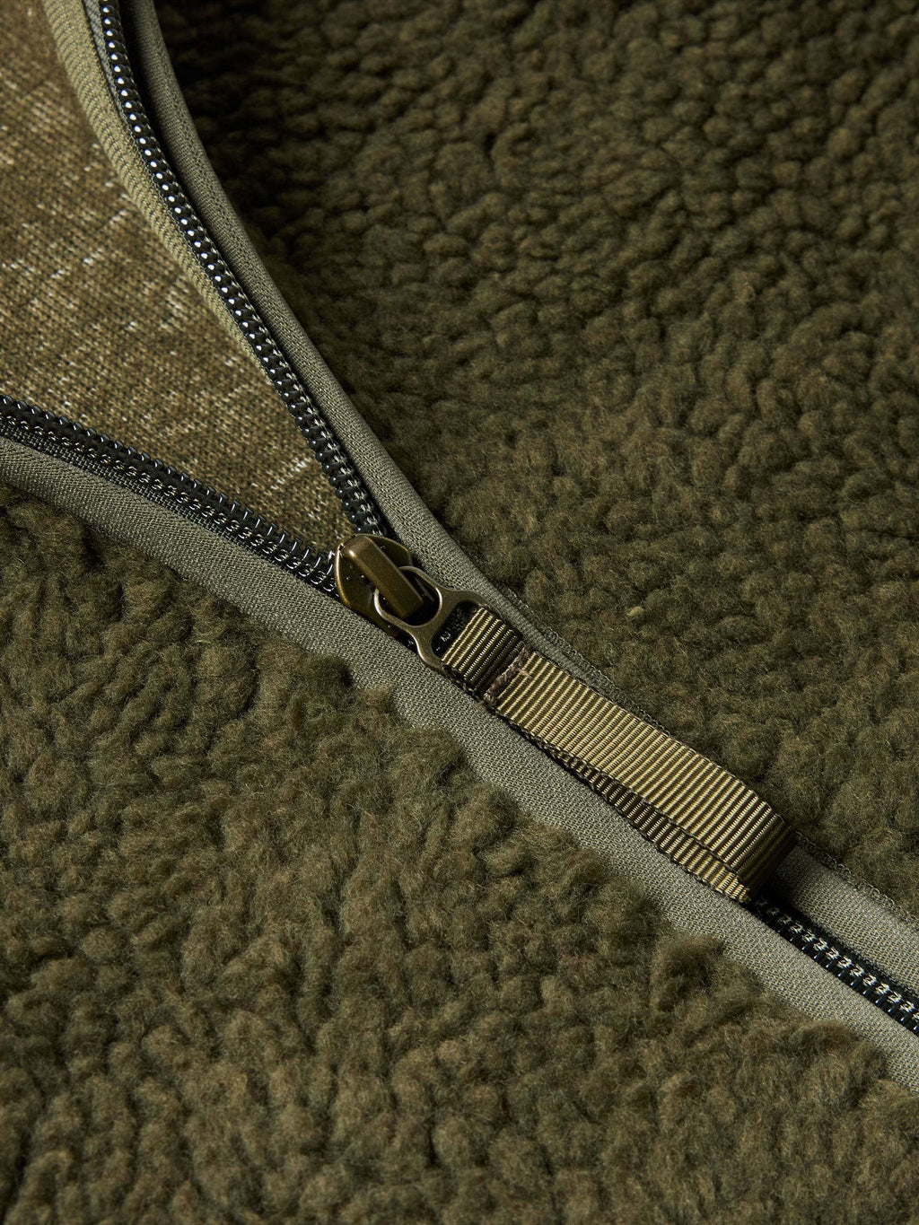 Olive zipper close-up with metal pull and stitched zipper tape on fleece jacket.