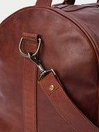 Russet leather duffel strap with brass D-ring and swivel clasp hardware detail.