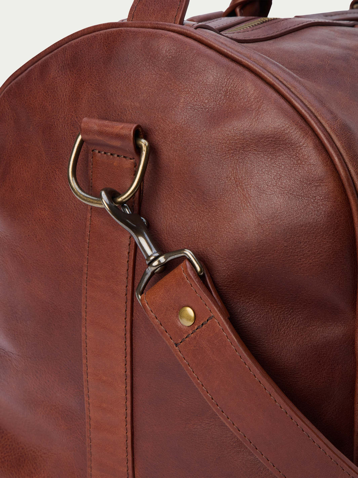 Russet leather duffel strap with brass D-ring and swivel clasp hardware detail.