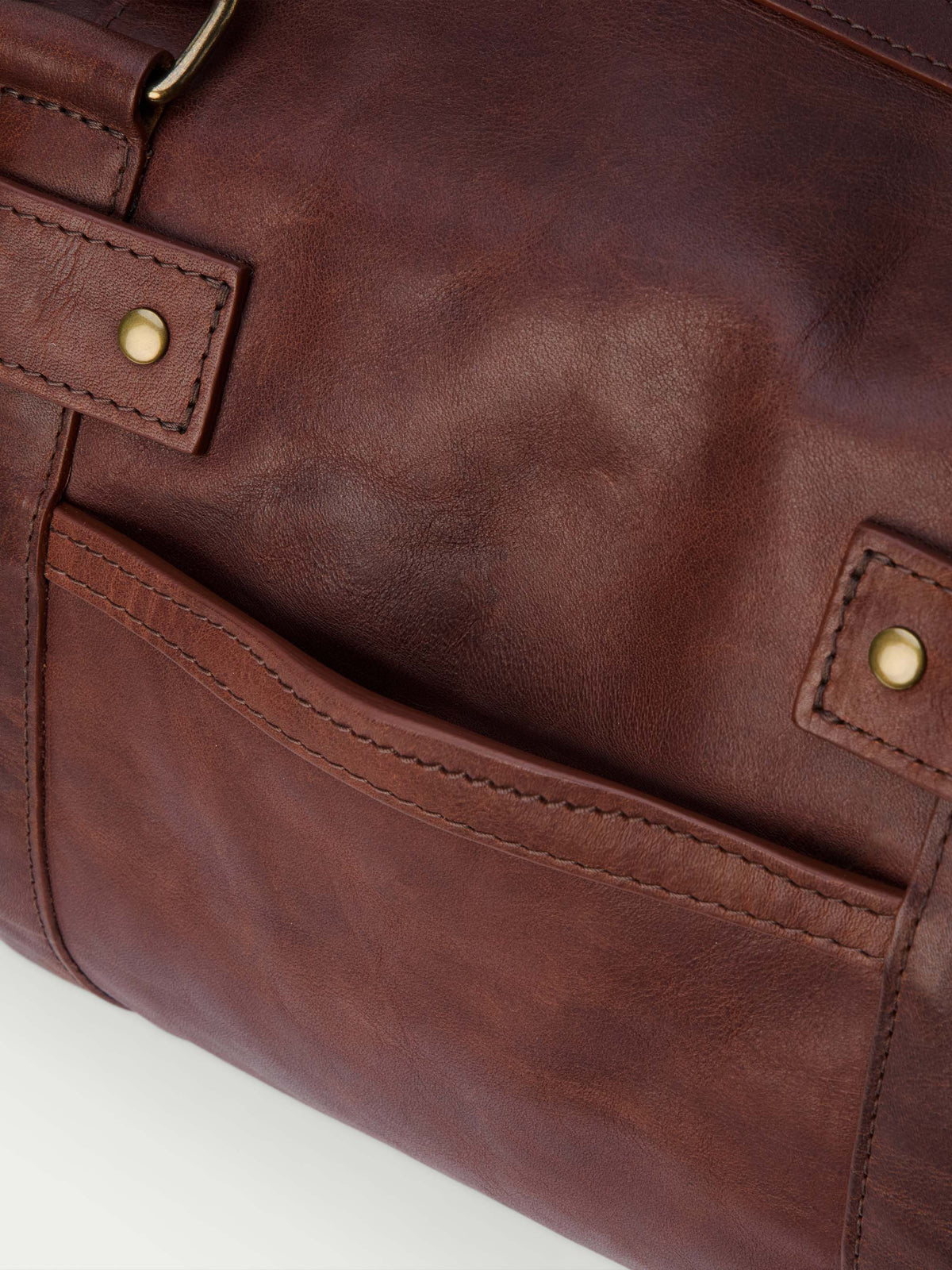 Russet leather duffel side pocket with brass snap button and contrast stitching.