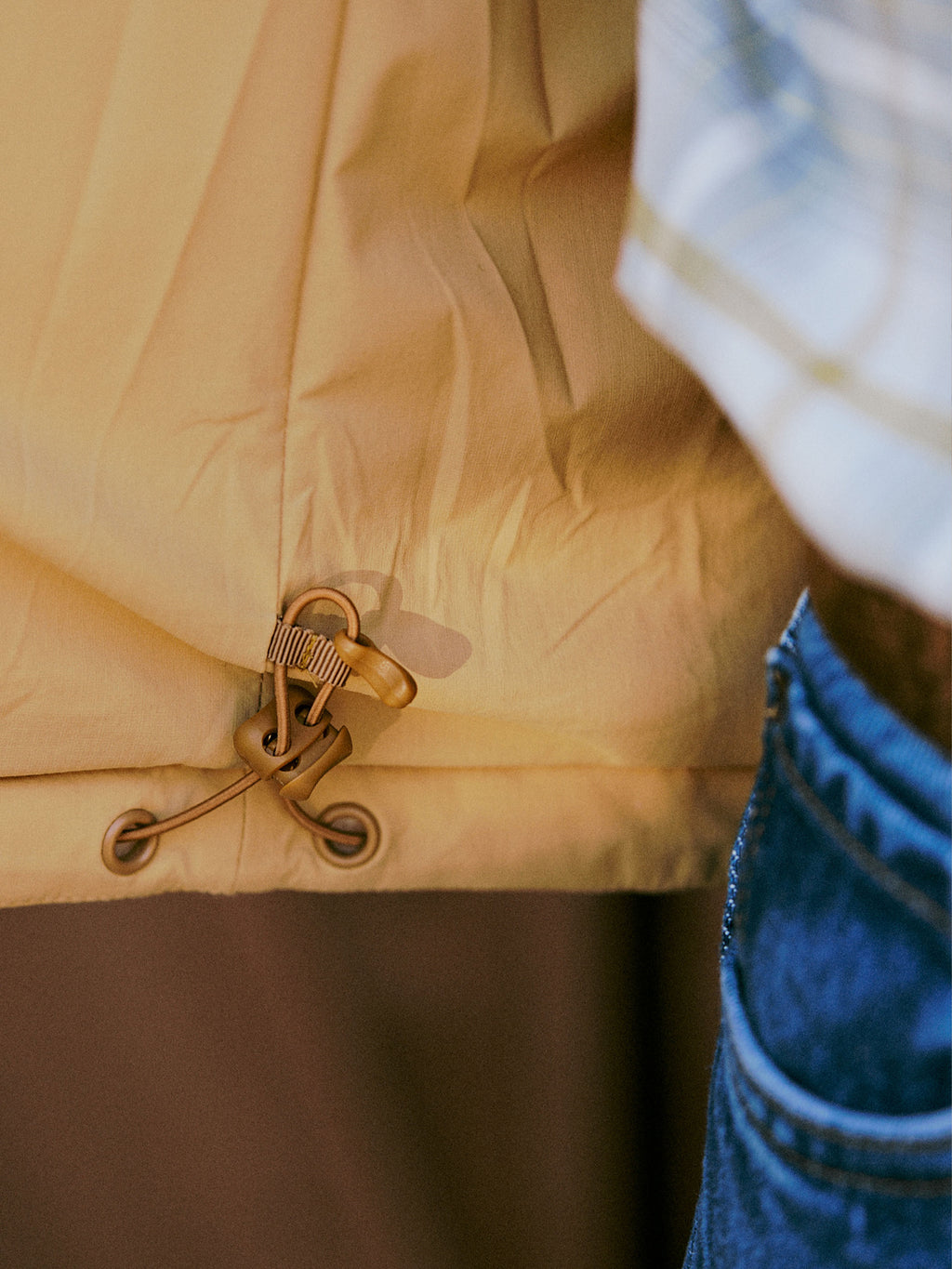 Tan vest hem with cord toggles and internal pocket opening detail