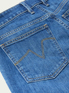 Medium-wash jeans close-up: stitched front pocket with decorative seaming and rivets.