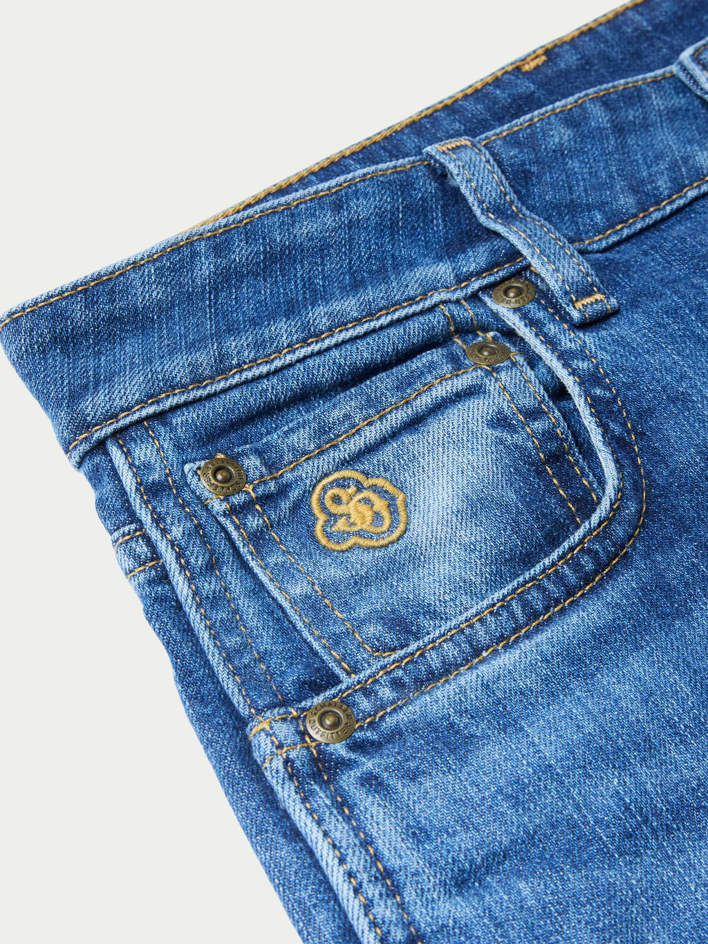 Medium-wash jeans detail: embroidered flower logo on back pocket with button flap.