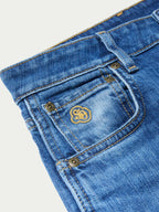 Medium-wash jeans detail: embroidered flower logo on back pocket with button flap.