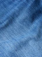 Medium-wash denim fabric close-up with textured weave and subtle whiskering.