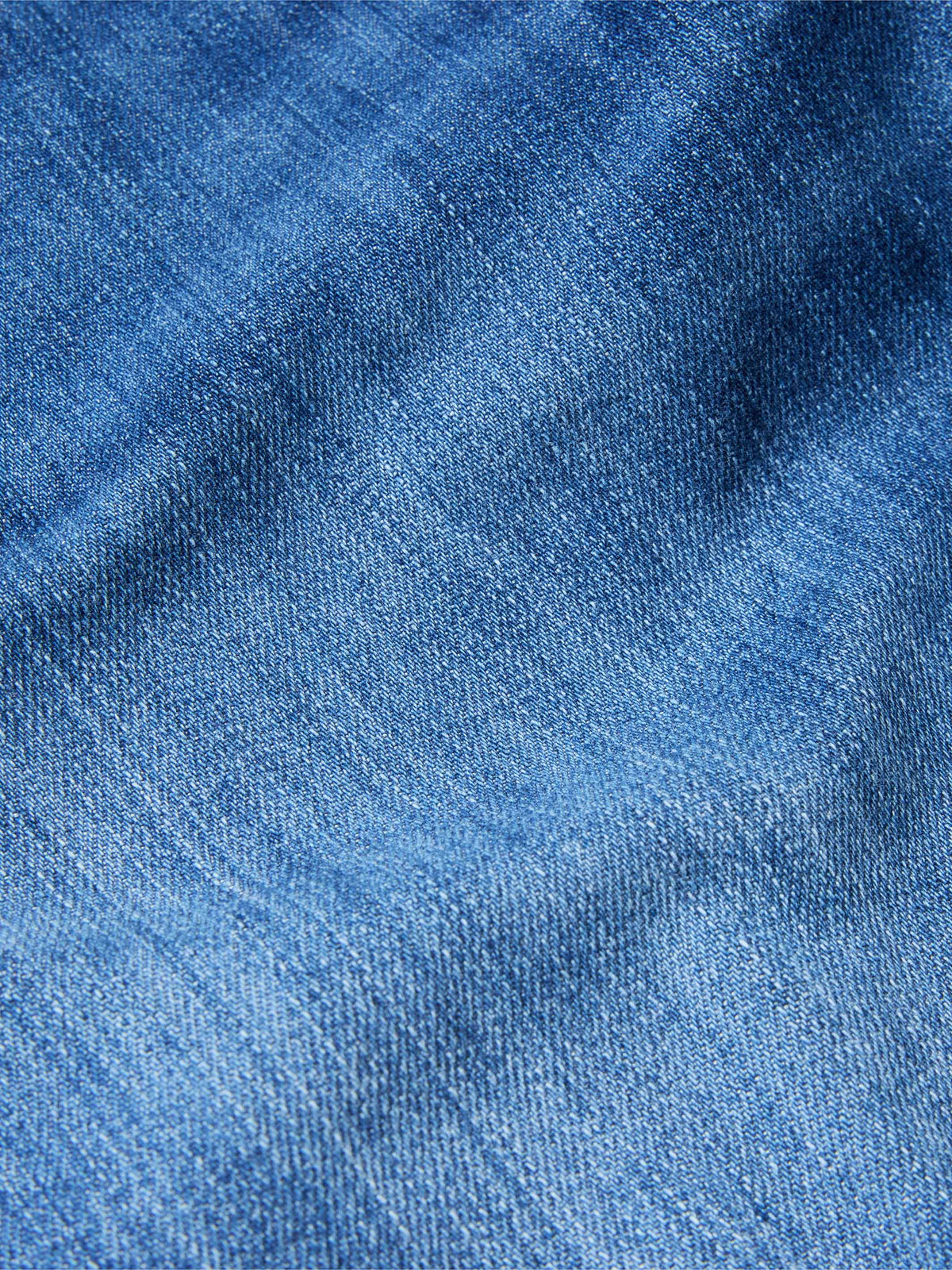 Medium-wash denim fabric close-up with textured weave and subtle whiskering.