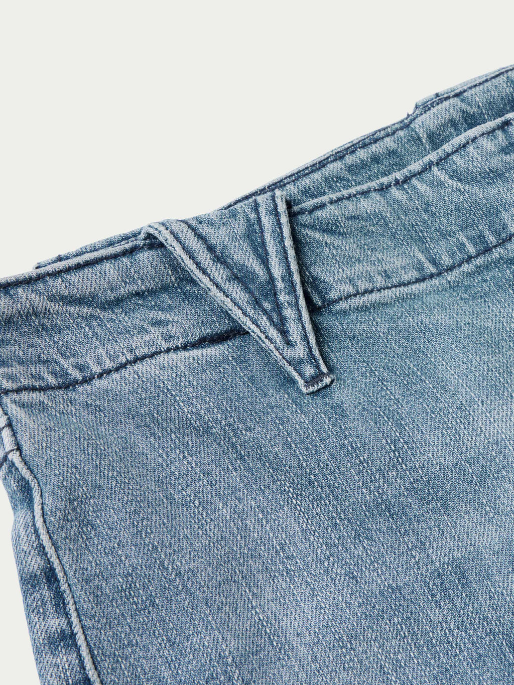 Medium wash denim jeans close-up of front rise and belt loop detail