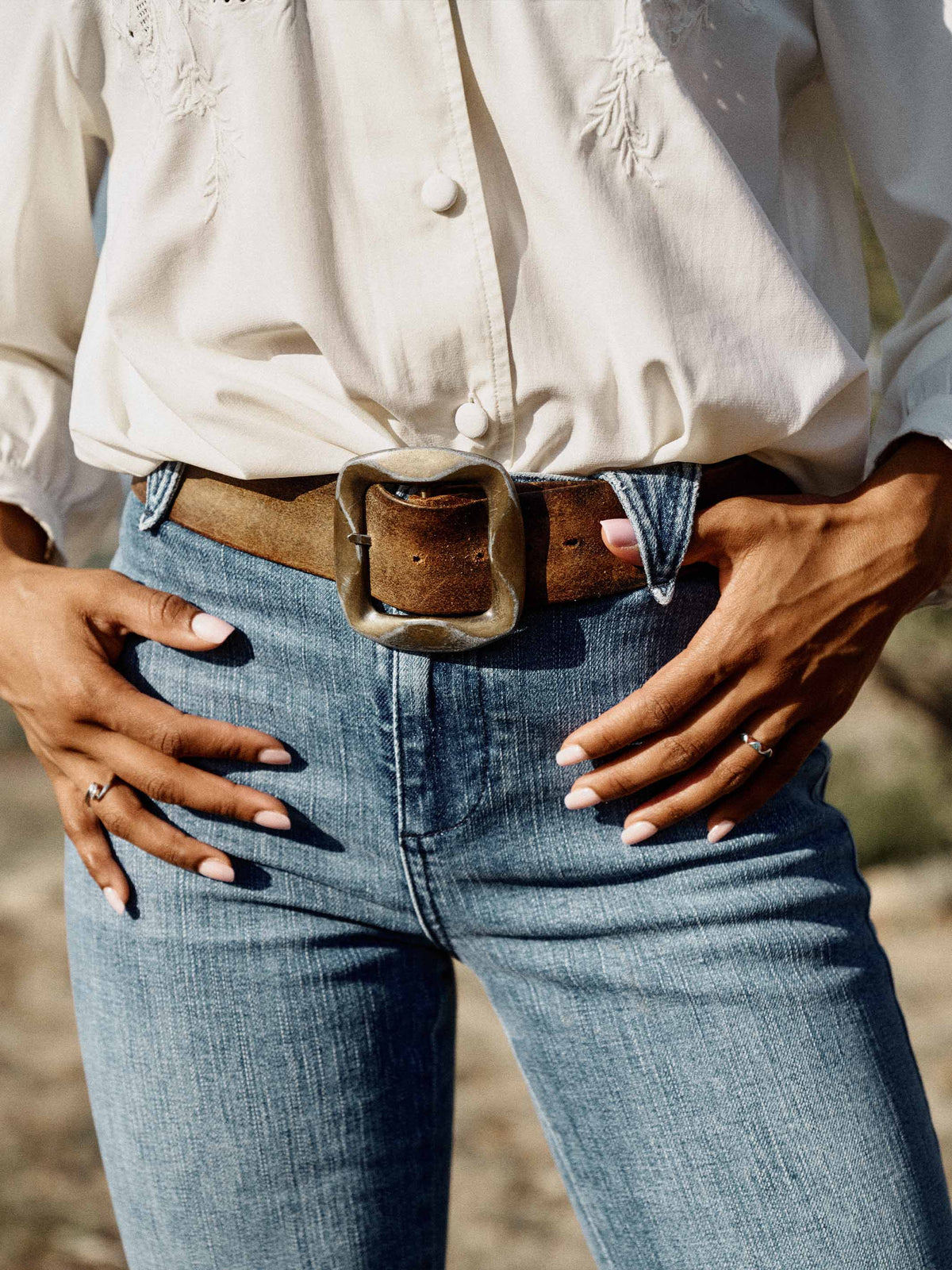 Medium wash denim jeans with belt loops, brown belt, and front button closure