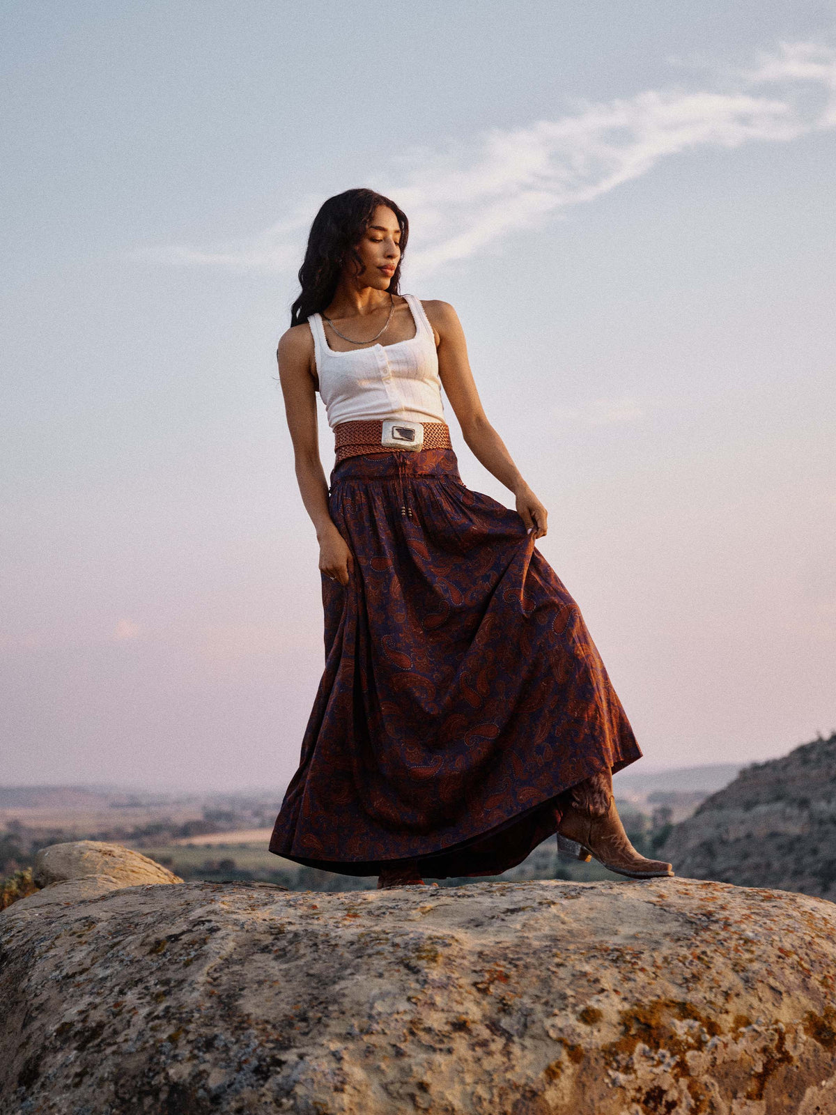 Paisley maxi skirt on model, dark blue base with rust-orange pattern and flared silhouette.