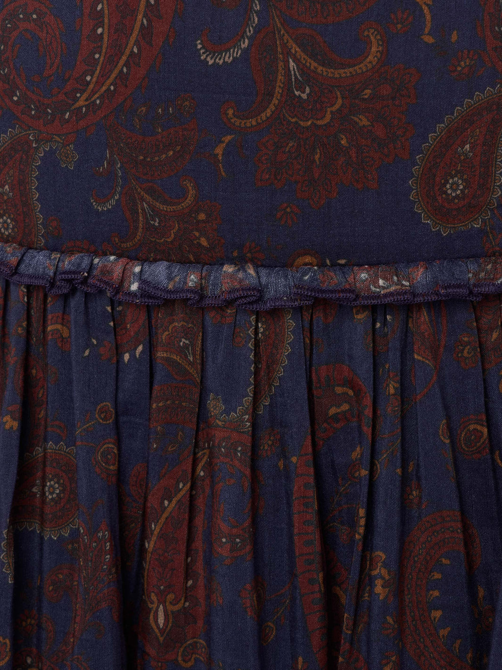Gathered skirt hem on dark blue paisley fabric with rust-orange swirling motifs.
