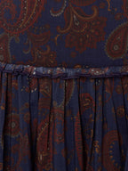 Gathered skirt hem on dark blue paisley fabric with rust-orange swirling motifs.