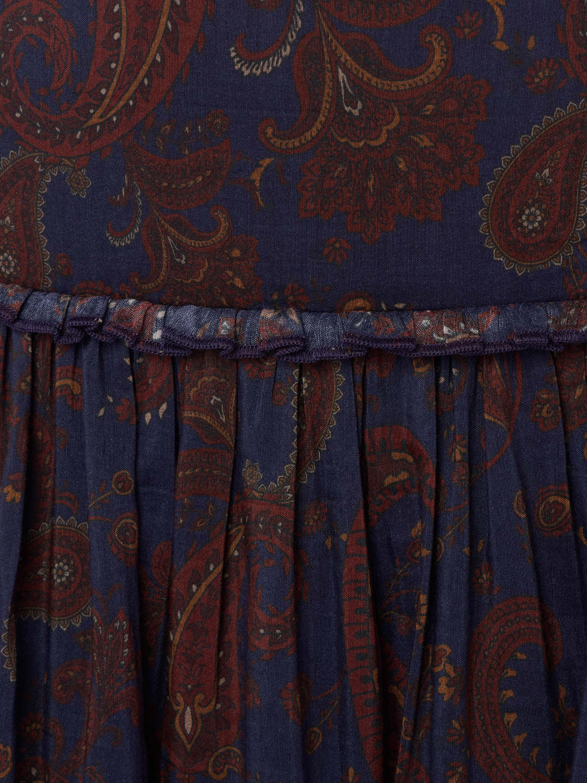 Gathered skirt hem on dark blue paisley fabric with rust-orange swirling motifs.