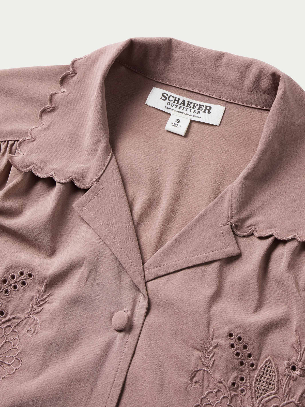 Washed plum blouse neckline close-up with brand label and scalloped cuff trim