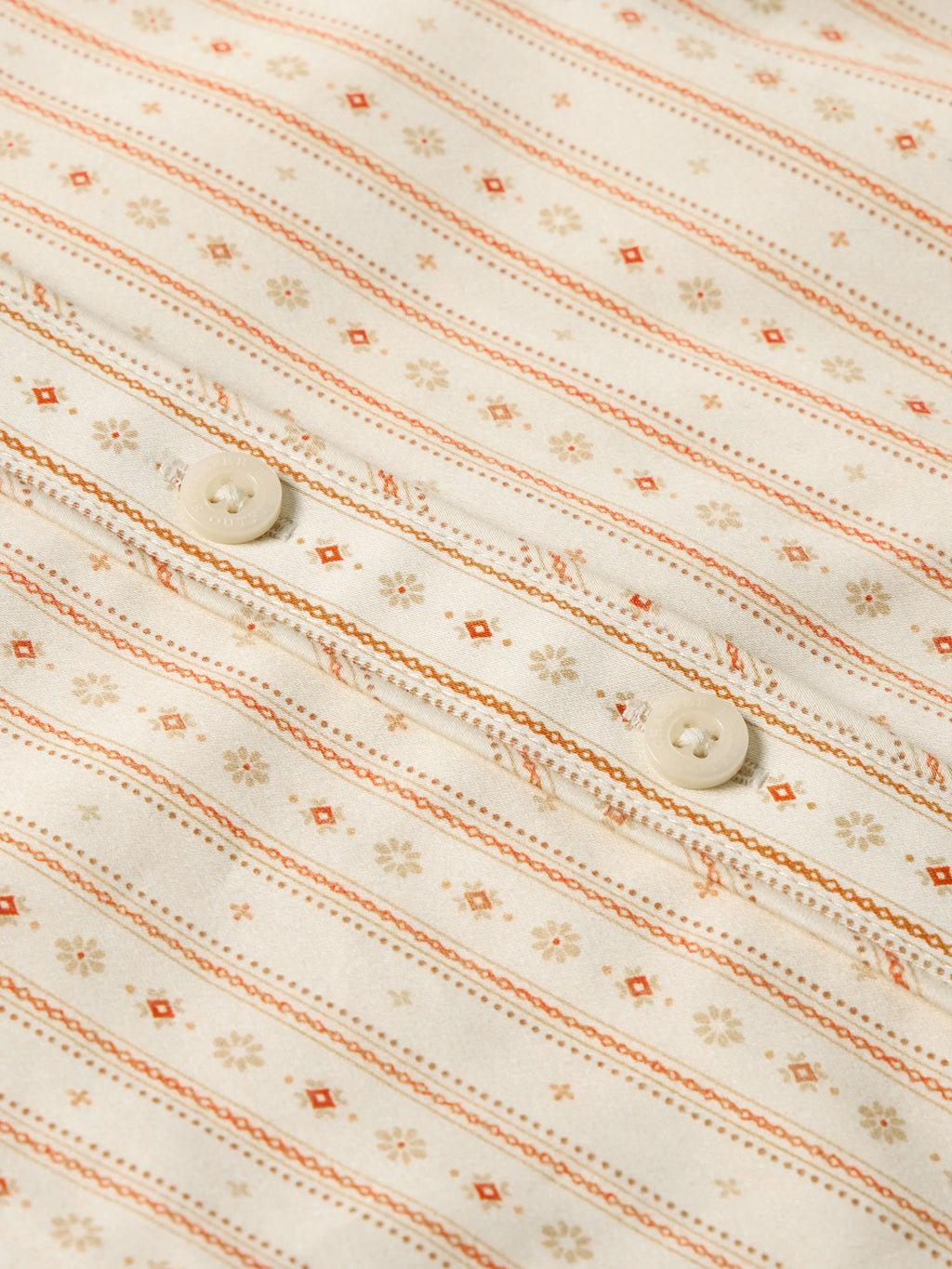Women's printed button-up shirt fabric detail with orange striped and floral motifs
