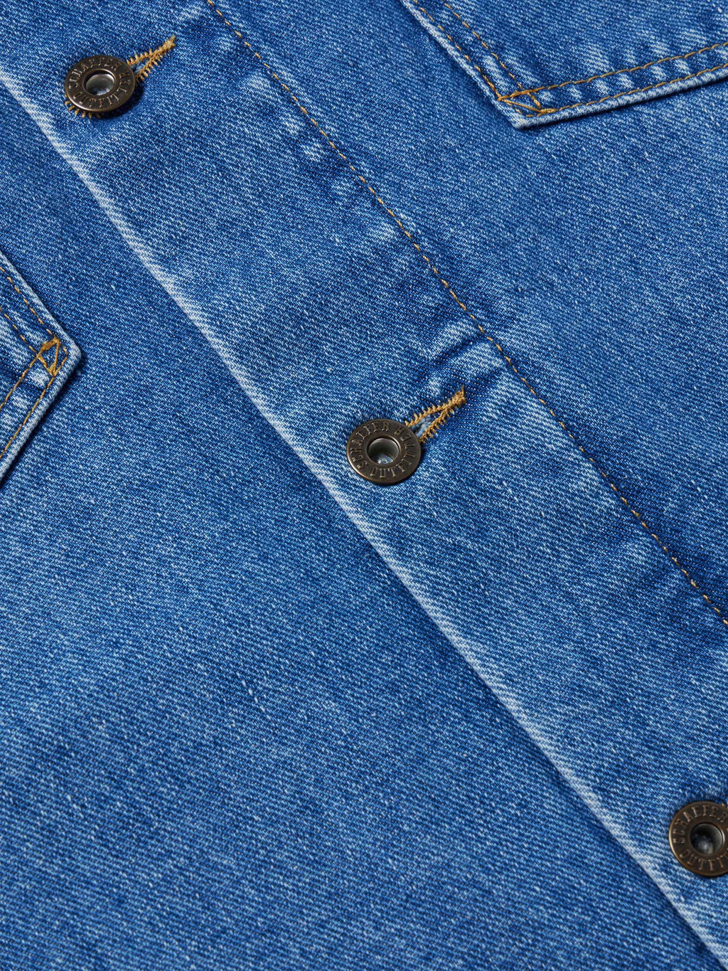 Close-up of indigo denim jacket placket with round metal snaps and tan stitching