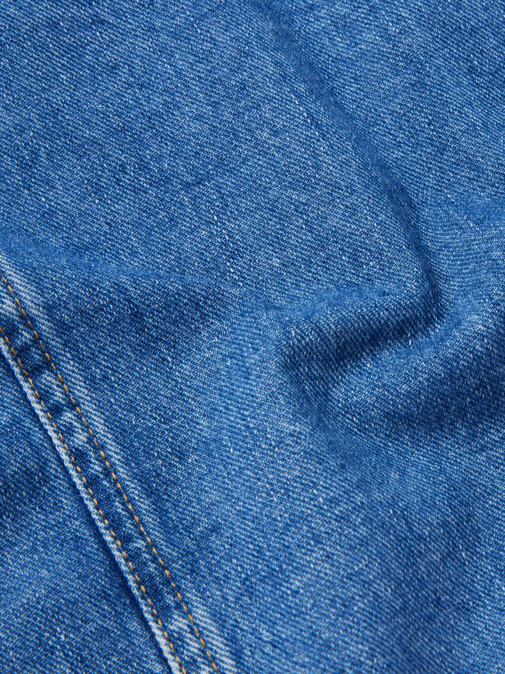 Close-up texture of medium indigo denim with stitched seams and buttonhole detail