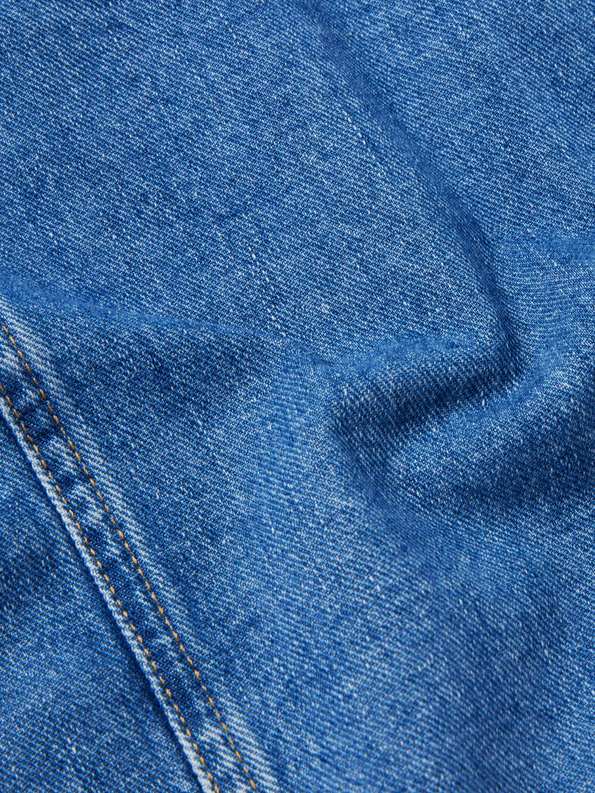 Close-up texture of medium indigo denim with stitched seams and buttonhole detail