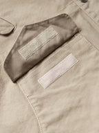 Beige coat pocket close-up with two snap-tab openings and contrast tabs