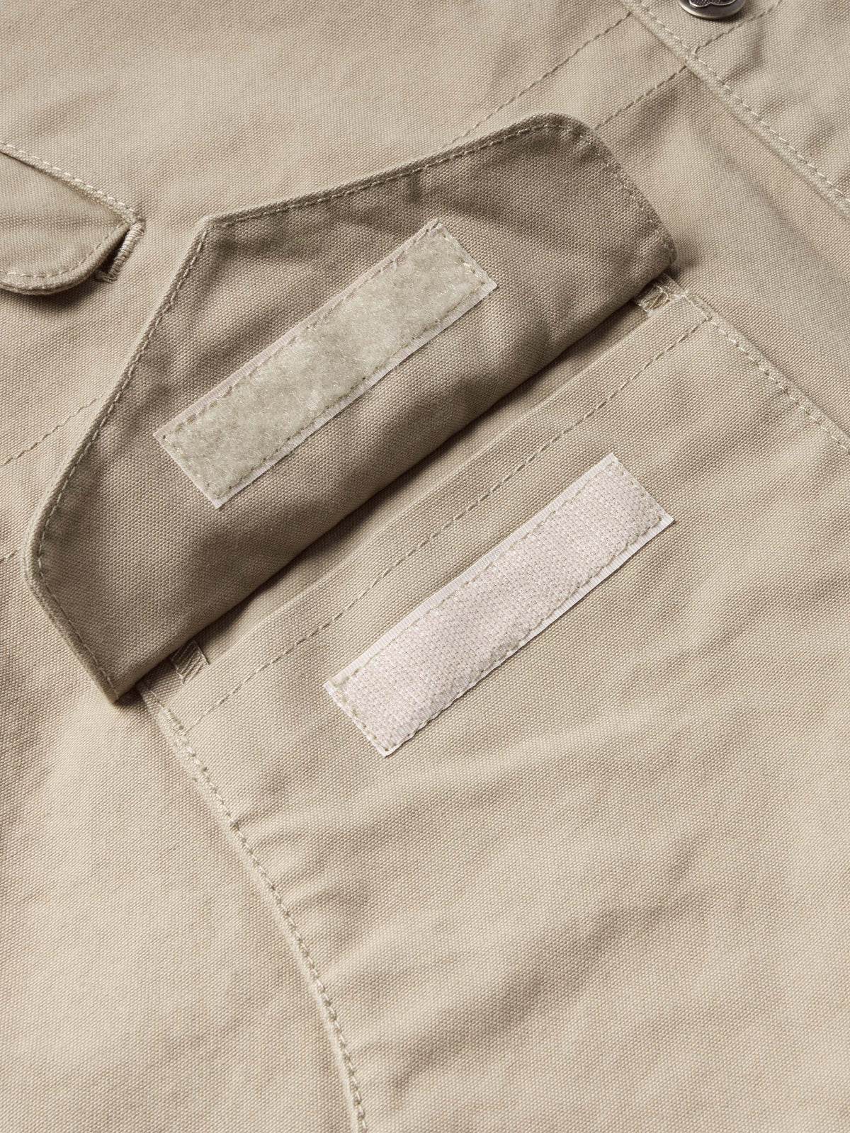 Beige coat pocket close-up with two snap-tab openings and contrast tabs