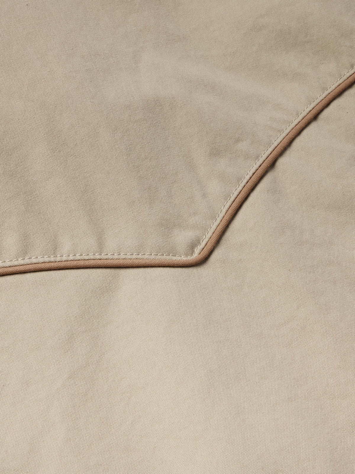 Beige coat fabric close-up with brown contrast piping and edge stitching